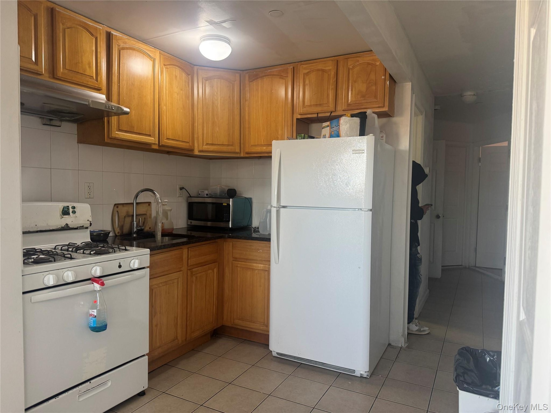 Kitchen with white appliances, light tile patterned floors, brown cabinetry, and backsplash