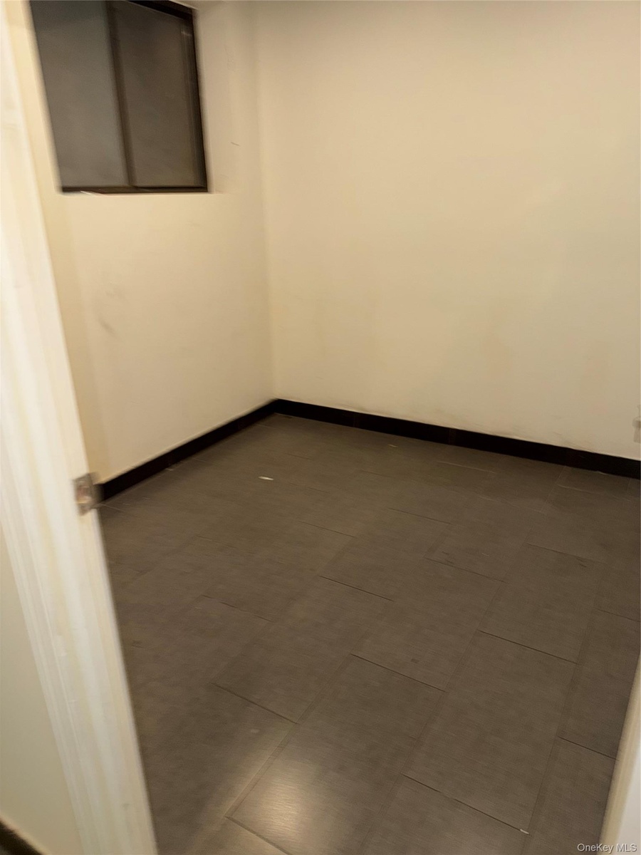 Compact room featuring light-colored walls, dark baseboards, and a window with a dark frame