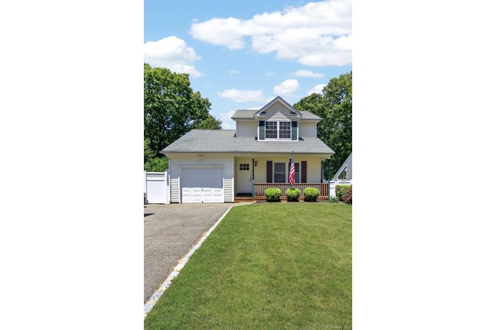 Two-story residence featuring a front porch with wood railing, an attached garage, a paved driveway, and a front lawn