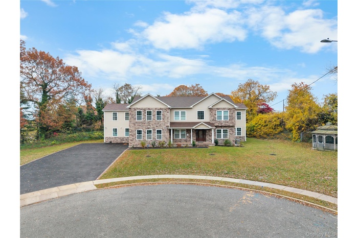 Traditional home with a porch, asphalt driveway, stone siding, and a front lawn