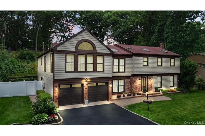 Two-story residence featuring light-toned siding with dark trim, a red-toned roofline with skylights, and a brick facade accent