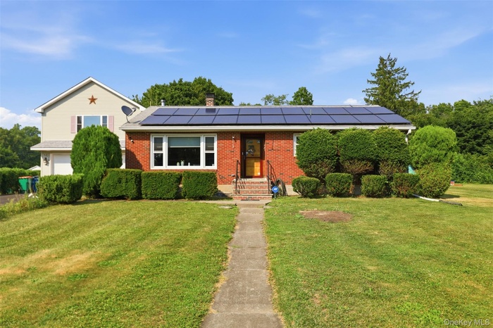 Brick facade home featuring solar panels and a landscaped front yard with a concrete walkway