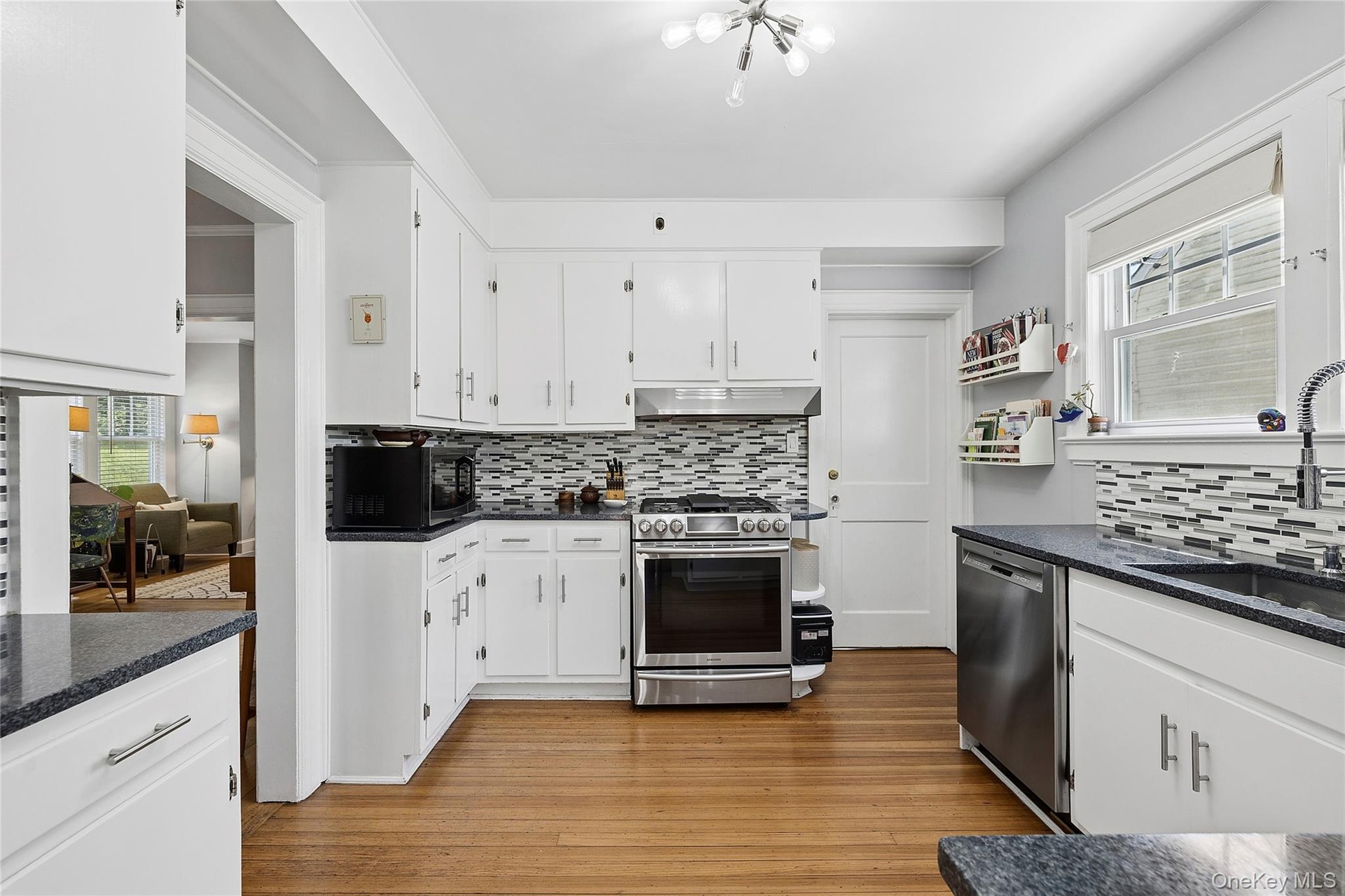 Kitchen featuring white cabinetry, dark speckled countertops, wood-finish flooring, a mosaic tile backsplash, and stainless steel appliances