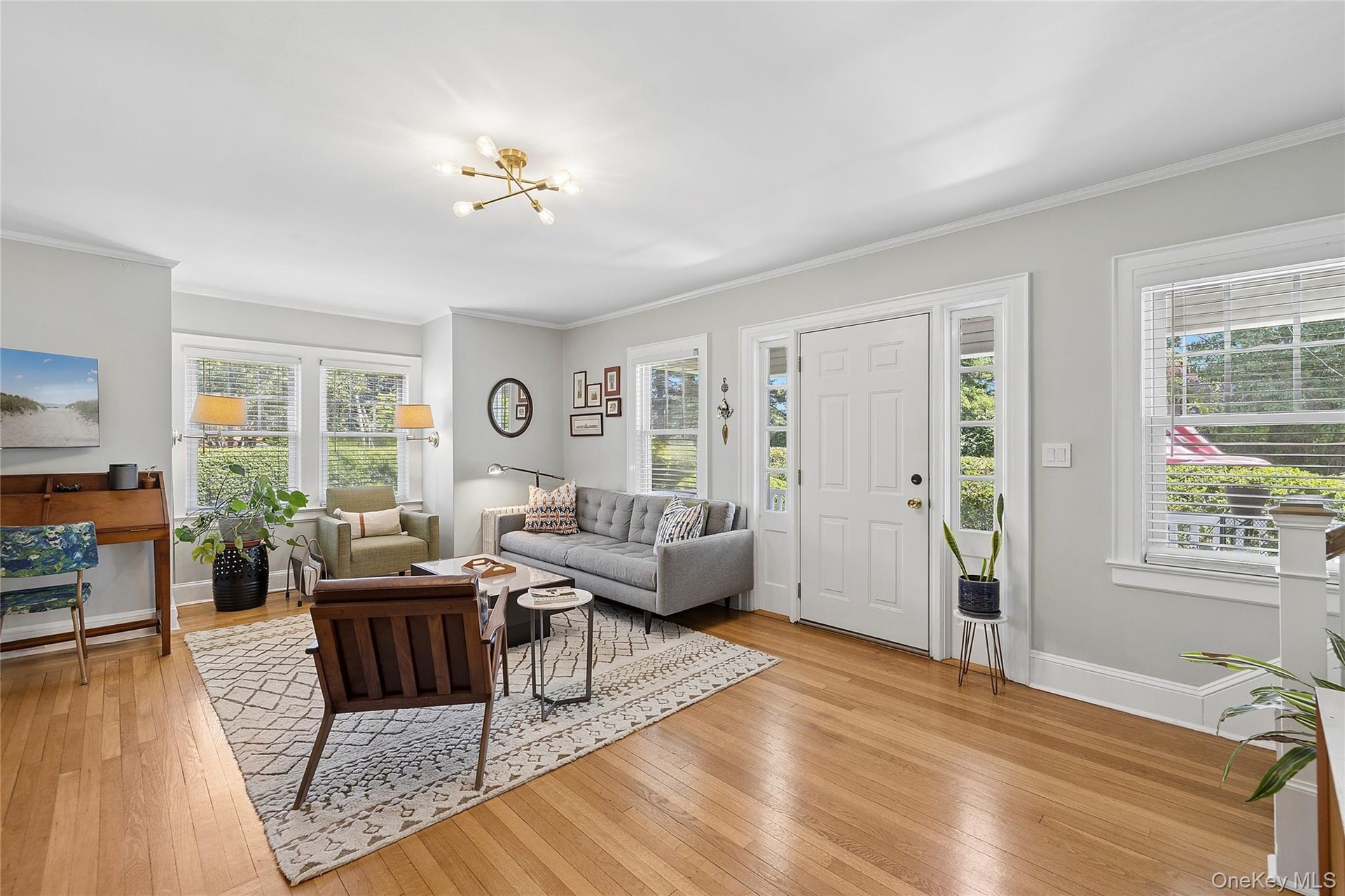 Light-filled living area featuring wood-finish flooring, a contemporary chandelier, multiple windows with natural light, and a white paneled entry doo