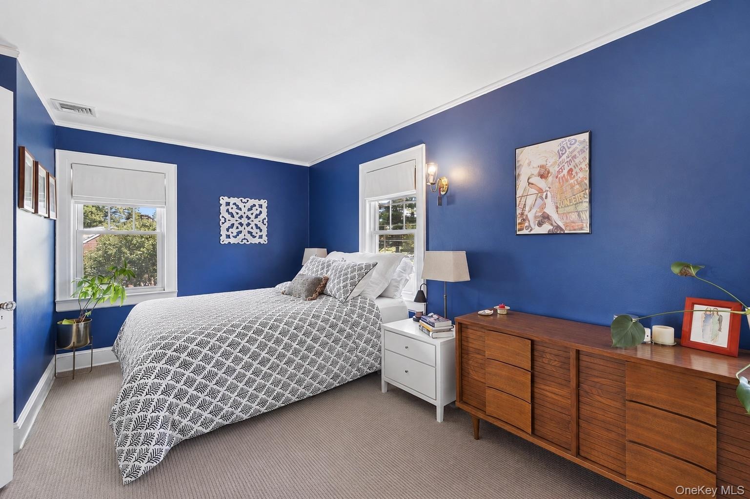 Carpeted room featuring two double-hung windows with white trim, a built-in wall sconce, and crown molding