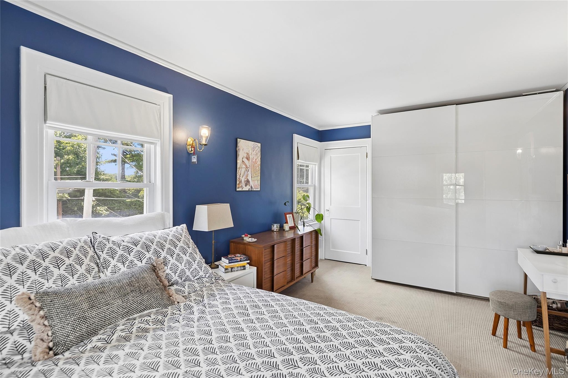 Bedroom featuring a window with white trim, a built-in wall sconce, a light-colored carpet, and a white sliding wardrobe system