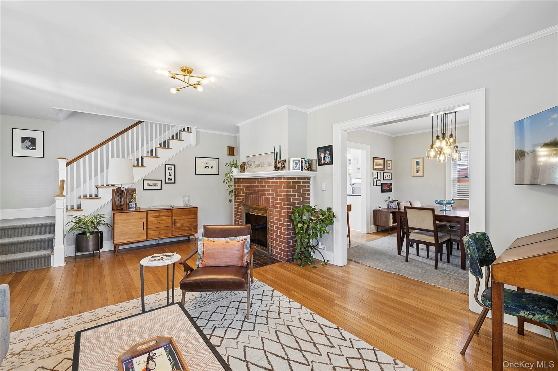 Spacious living area featuring warm wood-finish flooring, a white spindle staircase, and a brick fireplace