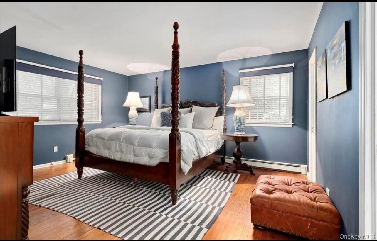 Bedroom with multiple windows, wood finished floors, and a baseboard radiator