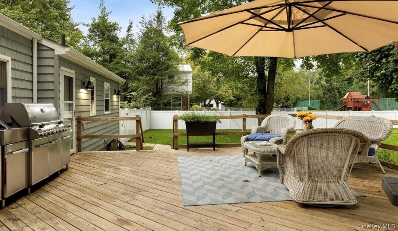 Wooden terrace with a fenced backyard, grilling area, outdoor dining space, and view of wooded area