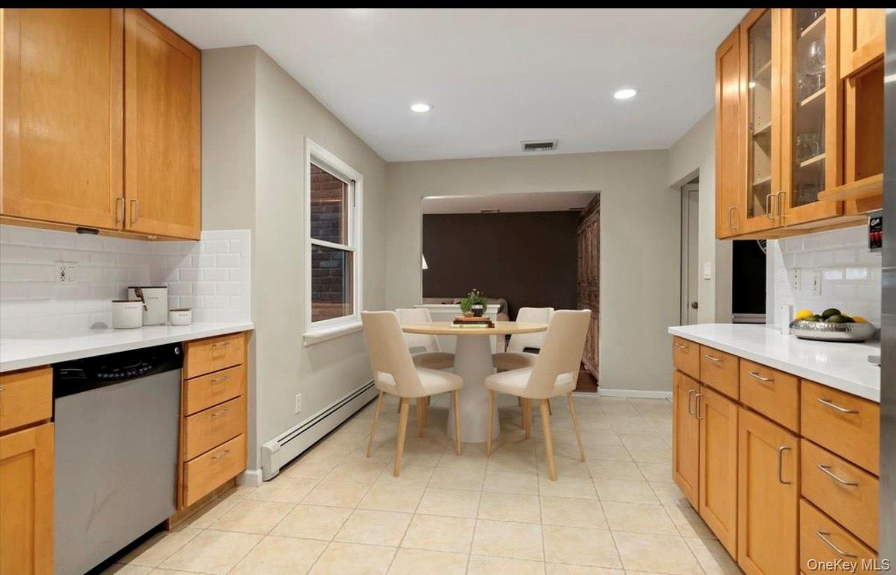 Kitchen featuring backsplash, a baseboard heating unit, stainless steel dishwasher, light countertops, and recessed lighting
