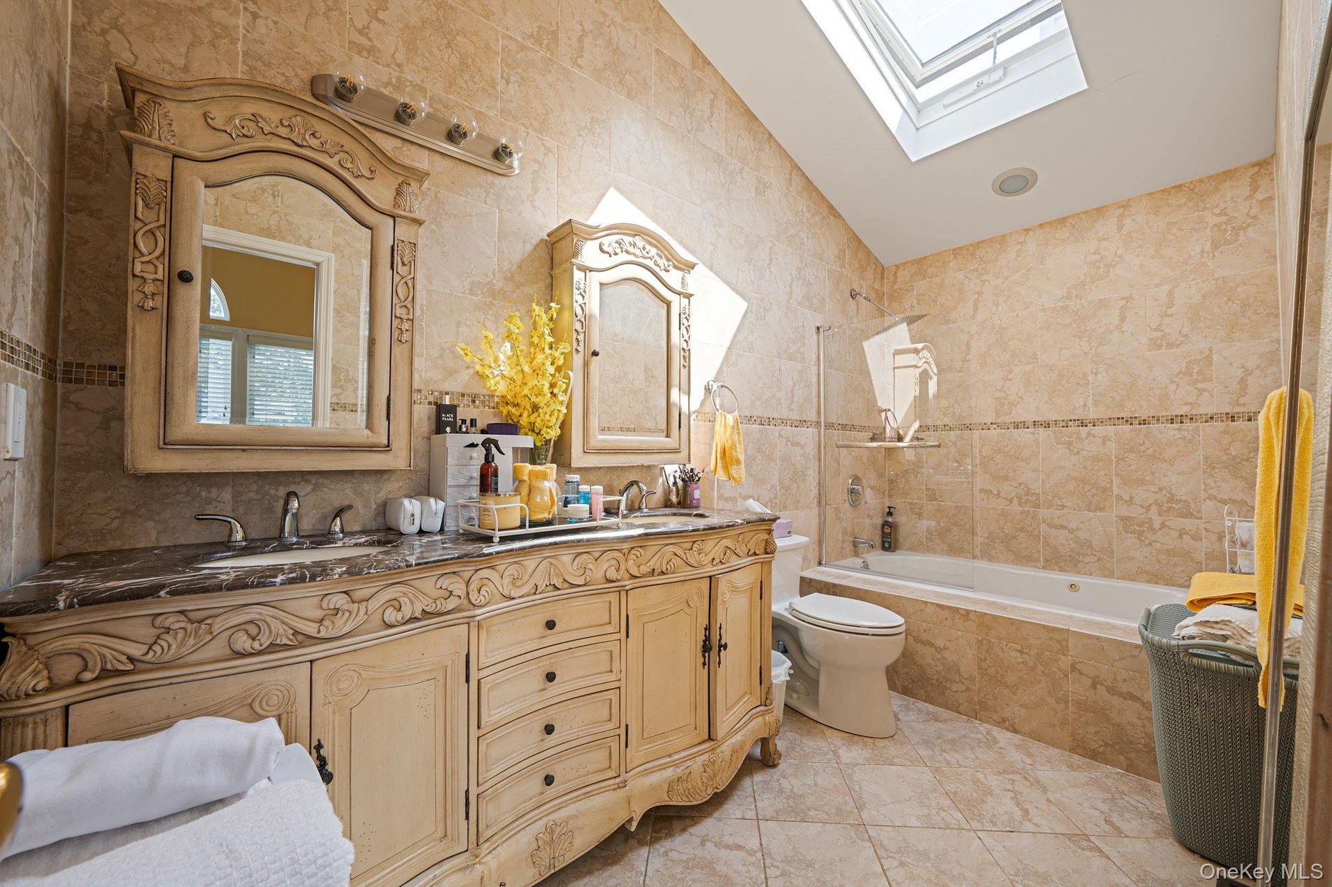 Bathroom featuring tile walls, a skylight, tiled shower / bath, double vanity, and vaulted ceiling