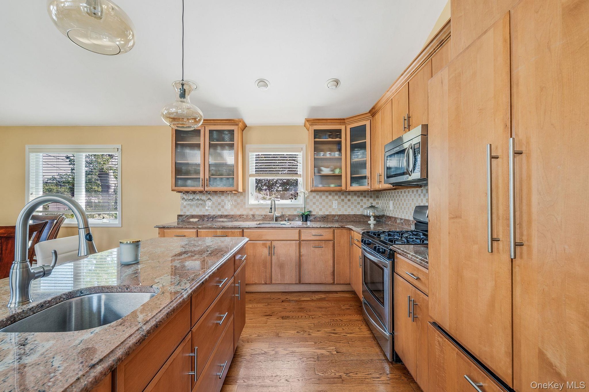 Kitchen with light wood-style floors, appliances with stainless steel finishes, glass insert cabinets, light stone countertops, and decorative light f