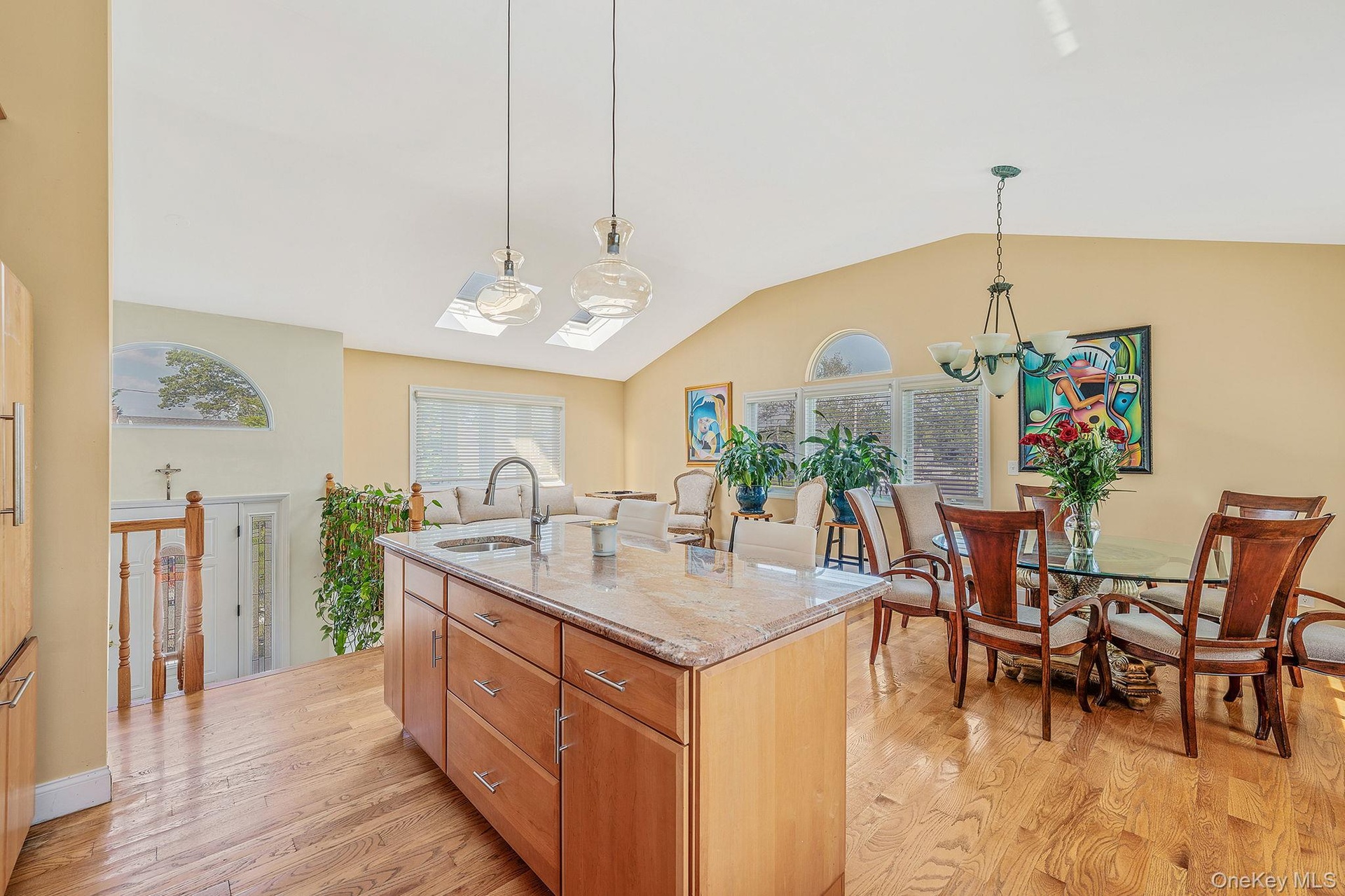 Kitchen with light stone counters, pendant lighting, light wood-style flooring, a kitchen island with sink, and a chandelier