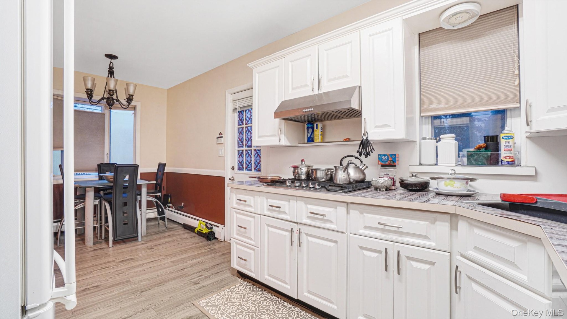 Kitchen featuring light countertops, white cabinetry, under cabinet range hood, and an inviting chandelier