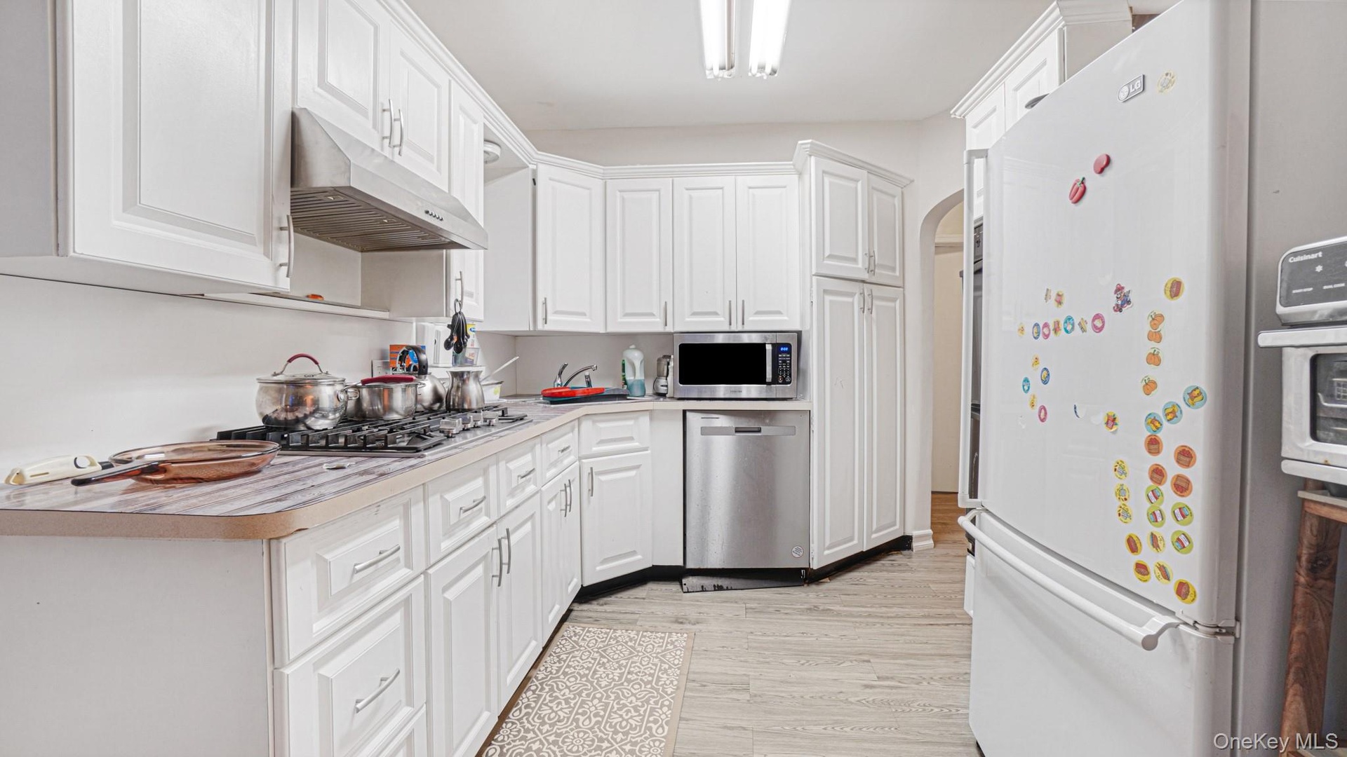Kitchen featuring under cabinet range hood, light countertops, light wood-style floors, appliances with stainless steel finishes, and white cabinetry