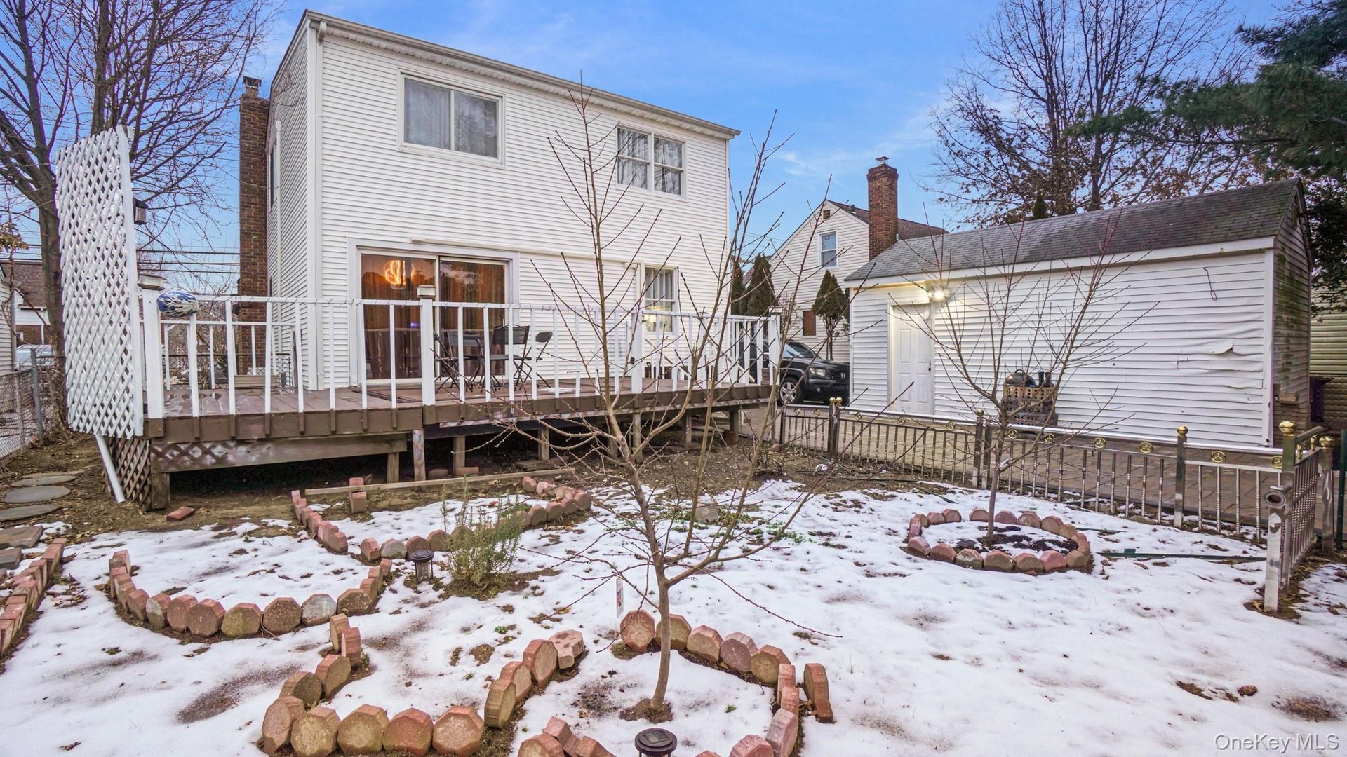Snow covered house with fence, a wooden deck, and a chimney