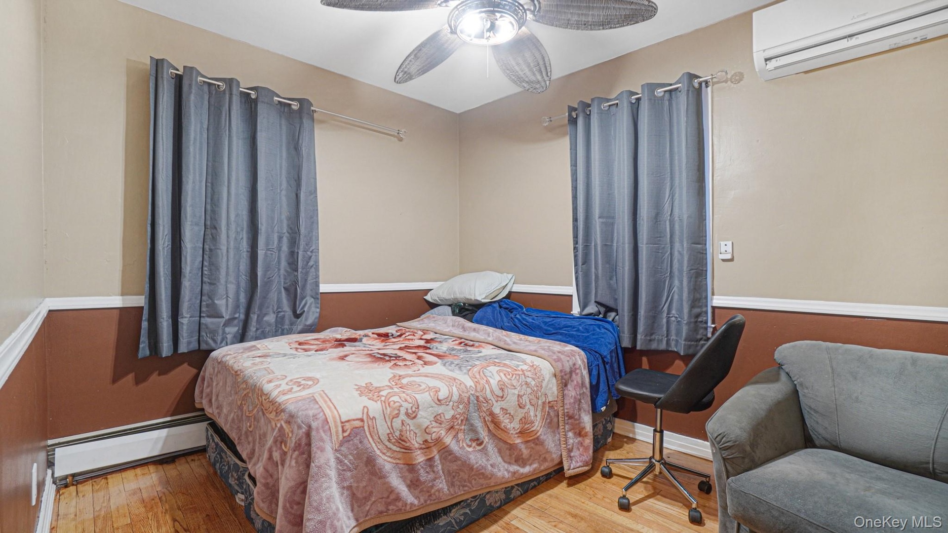 Bedroom featuring a baseboard heating unit, a ceiling fan, wood finished floors, and a wall mounted AC