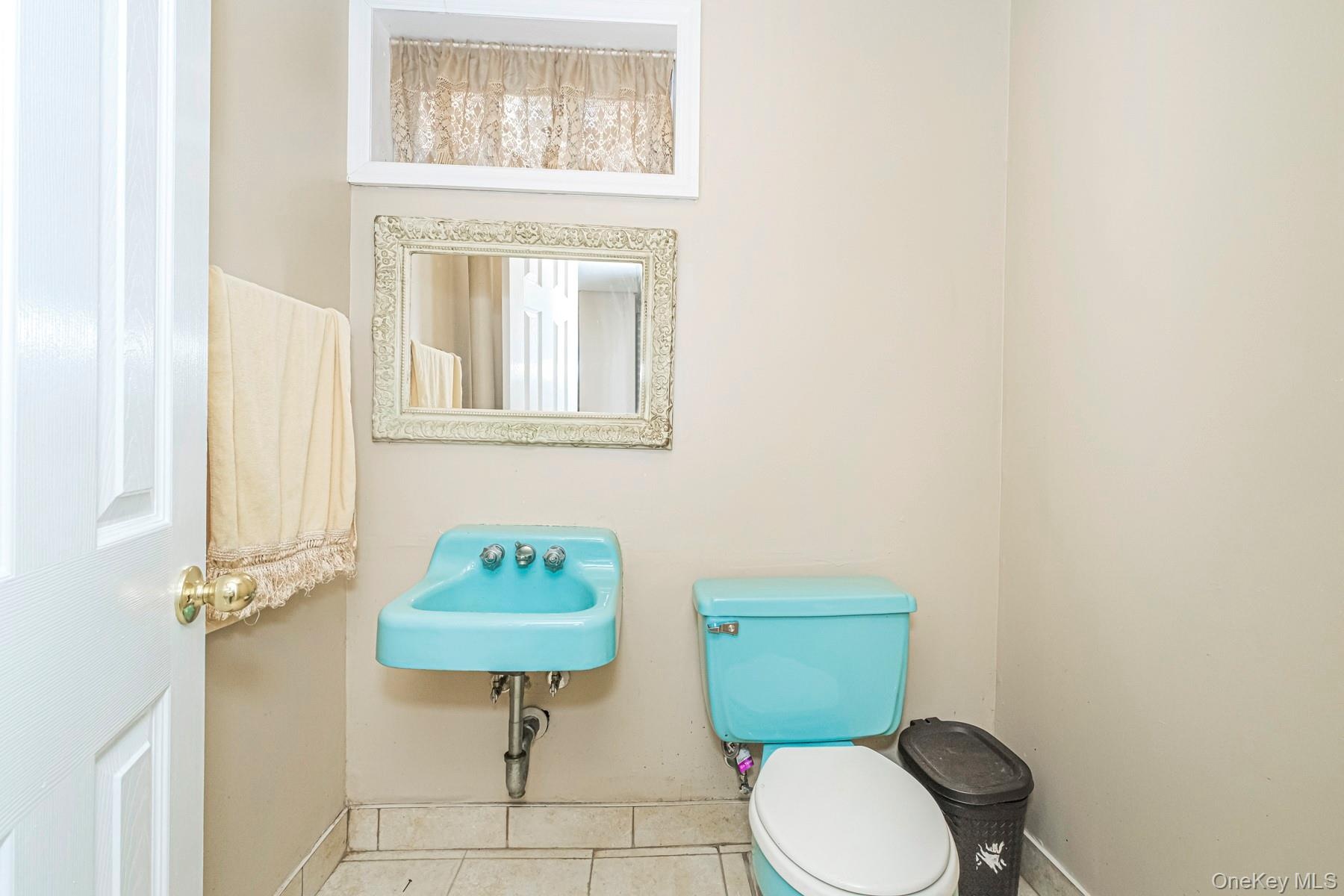 Bathroom featuring a wall-mounted blue basin, matching blue toilet, an ornate framed mirror, and a small recessed window