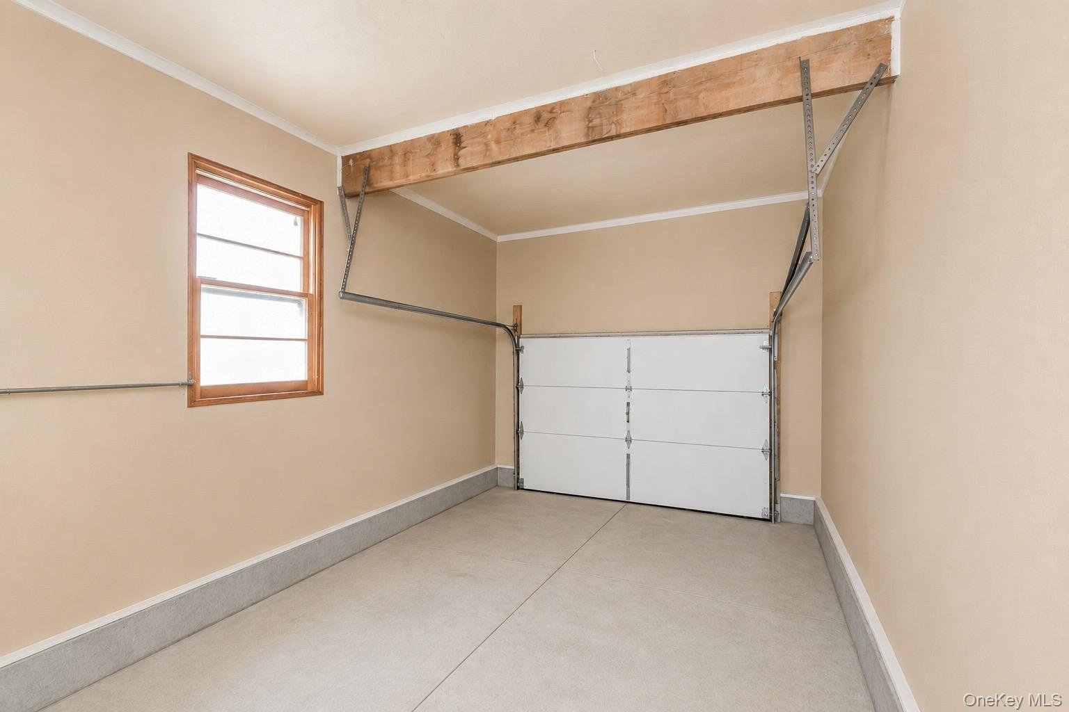 Garage interior featuring a single window with wood framing, beige painted walls, crown molding, and a sectional overhead door
