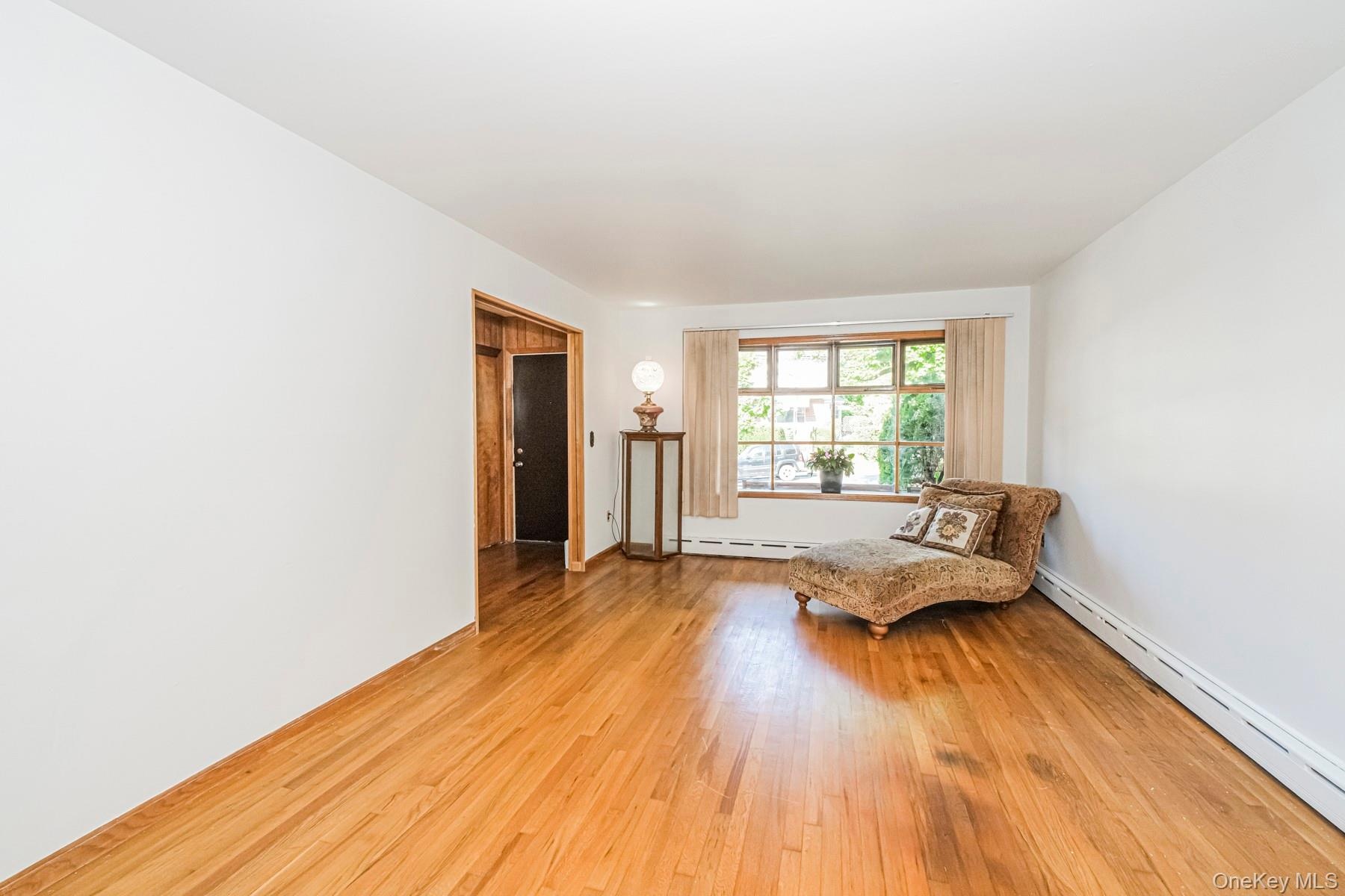 Spacious room featuring wood-finish flooring, a large multi-pane window with natural light, and perimeter baseboard heating
