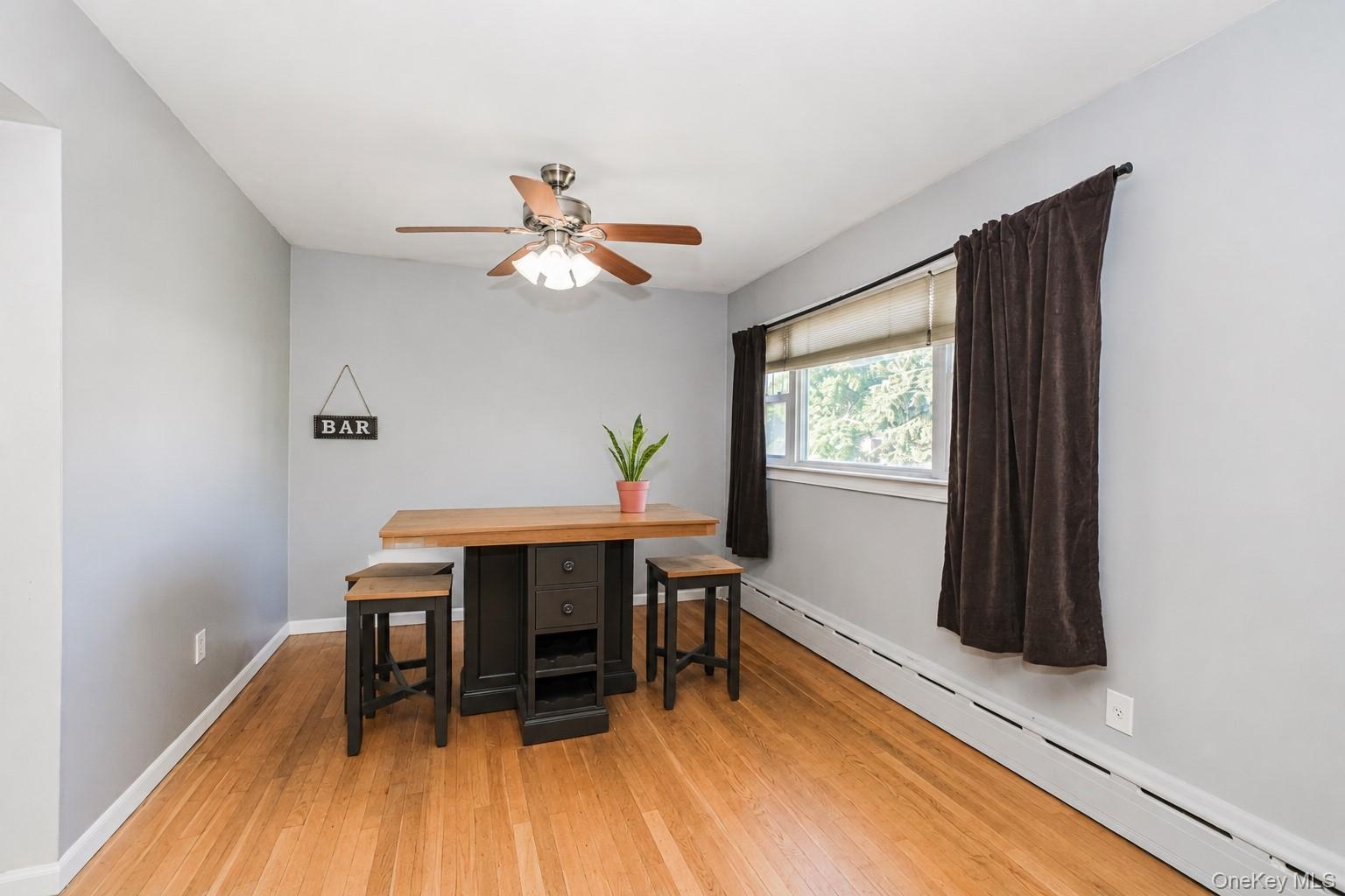 Hardwood flooring throughout featuring light gray walls, a window with natural light, and a ceiling fan with integrated lighting