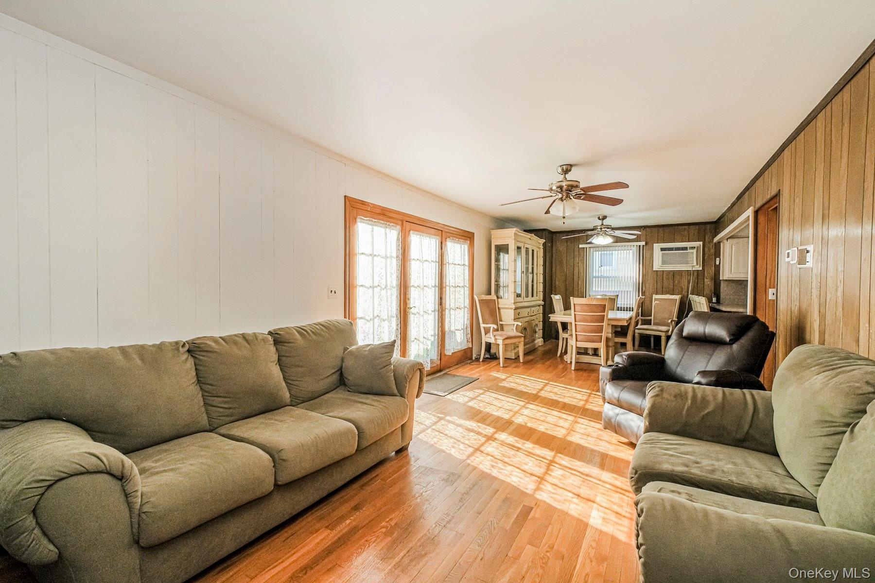 Open-concept living area with wood-finish flooring, white vertical paneled wall, and a wood-paneled accent wall
