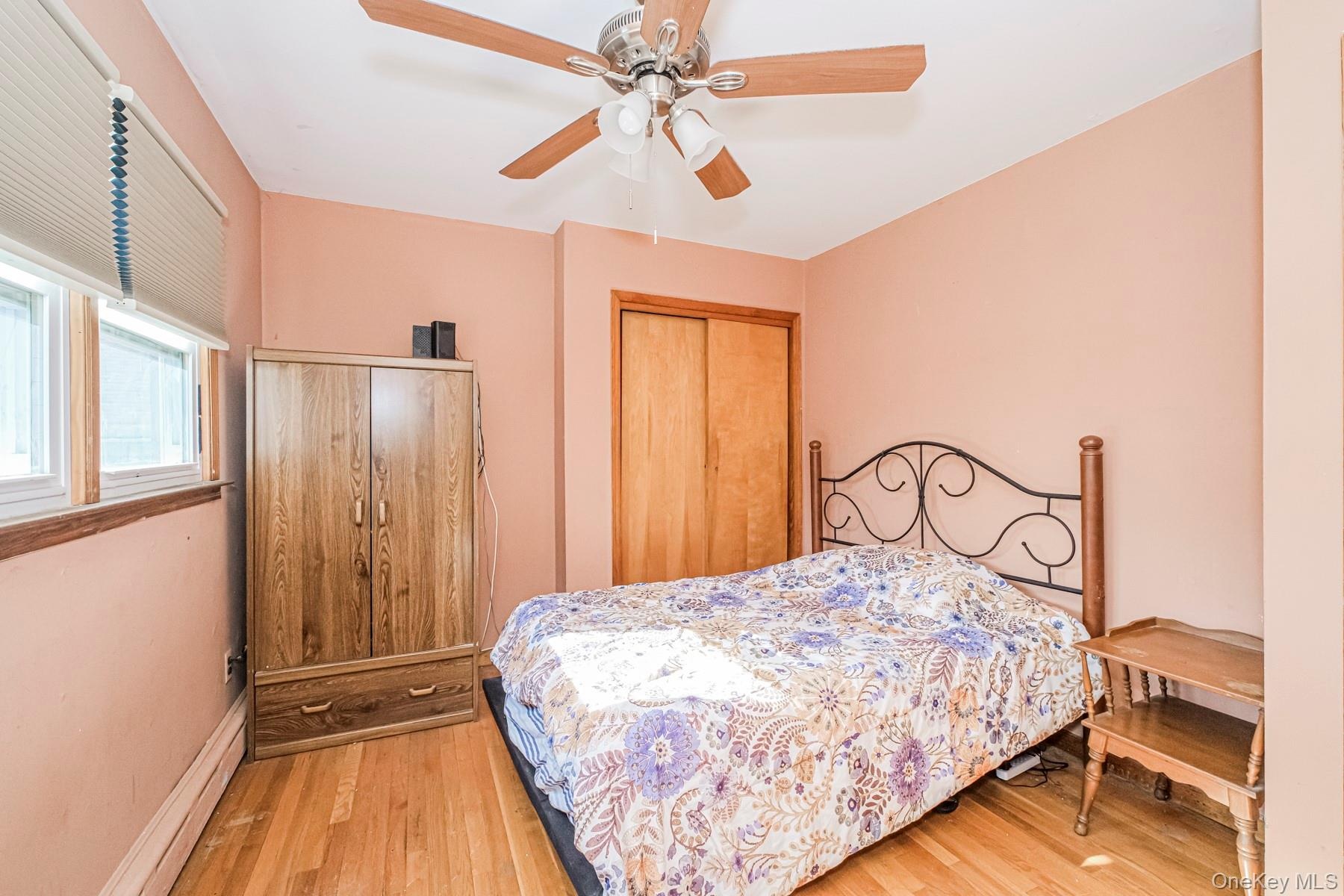 Room featuring wood-finish flooring, a ceiling fan with integrated lighting, and a window with blinds