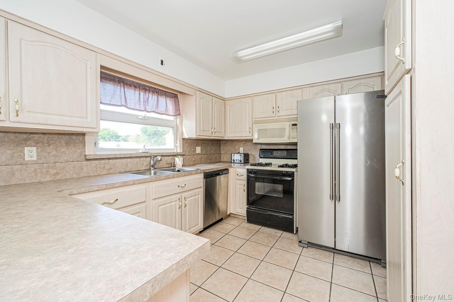 Kitchen featuring light-toned cabinetry with brass hardware, a stainless steel side-by-side refrigerator, a black electric range, and a stainless stee
