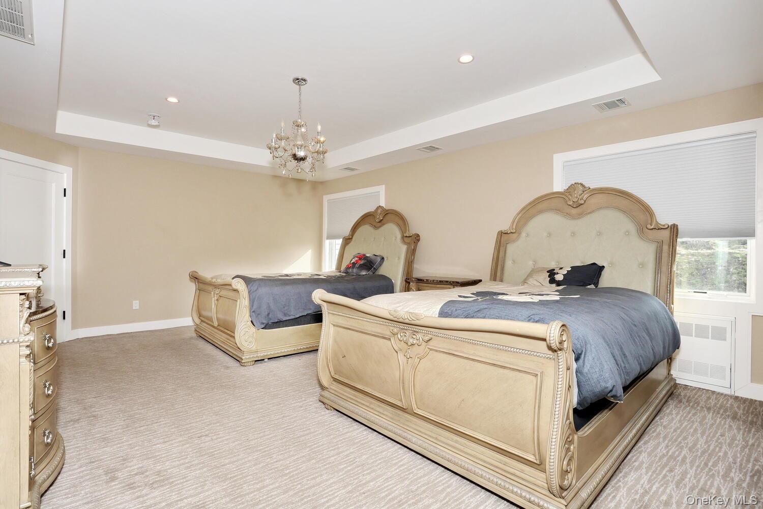 Bedroom featuring a tray ceiling, recessed lighting, light carpet, radiator, and a chandelier