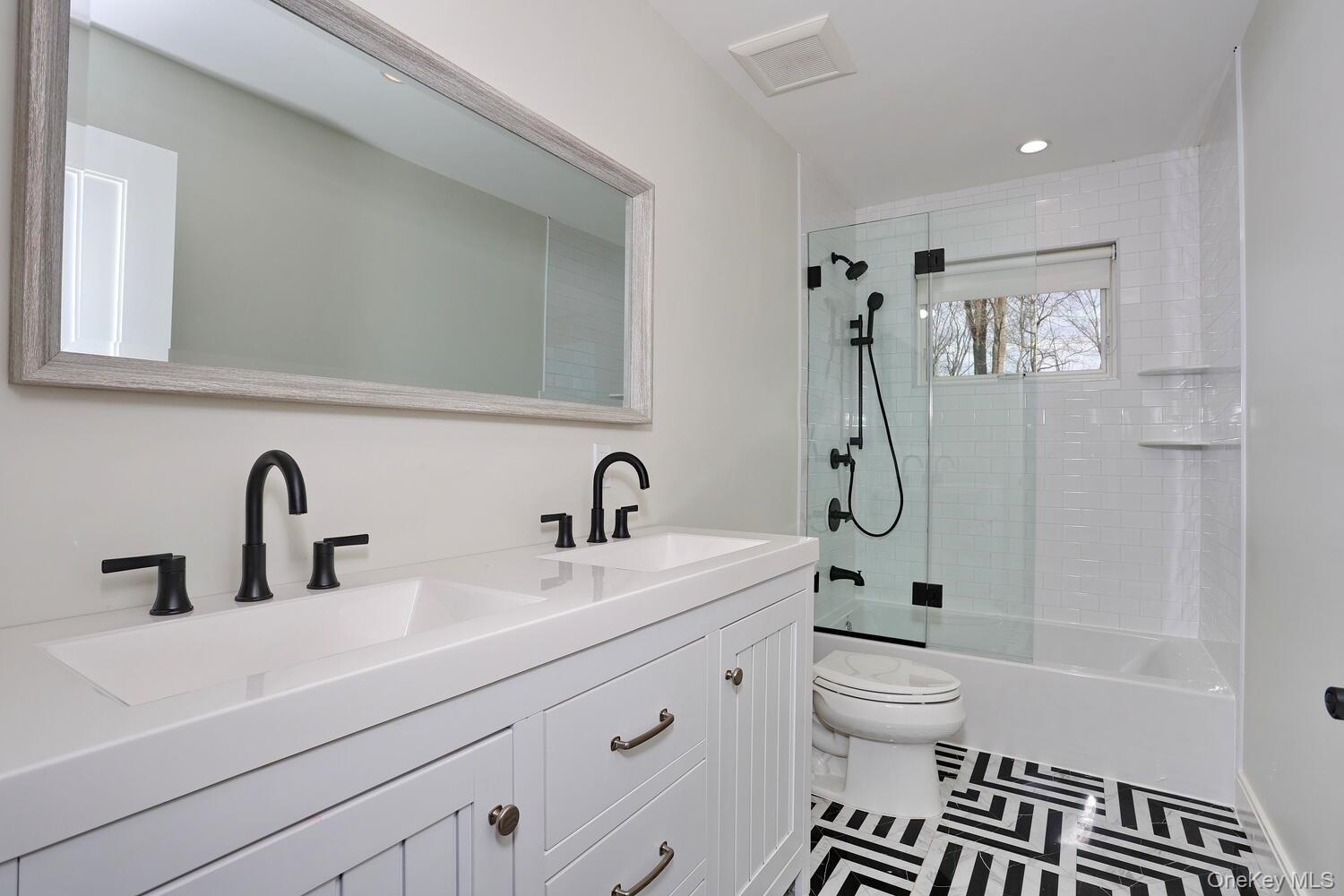 Bathroom featuring double vanity, combined bath / shower with glass door, and recessed lighting