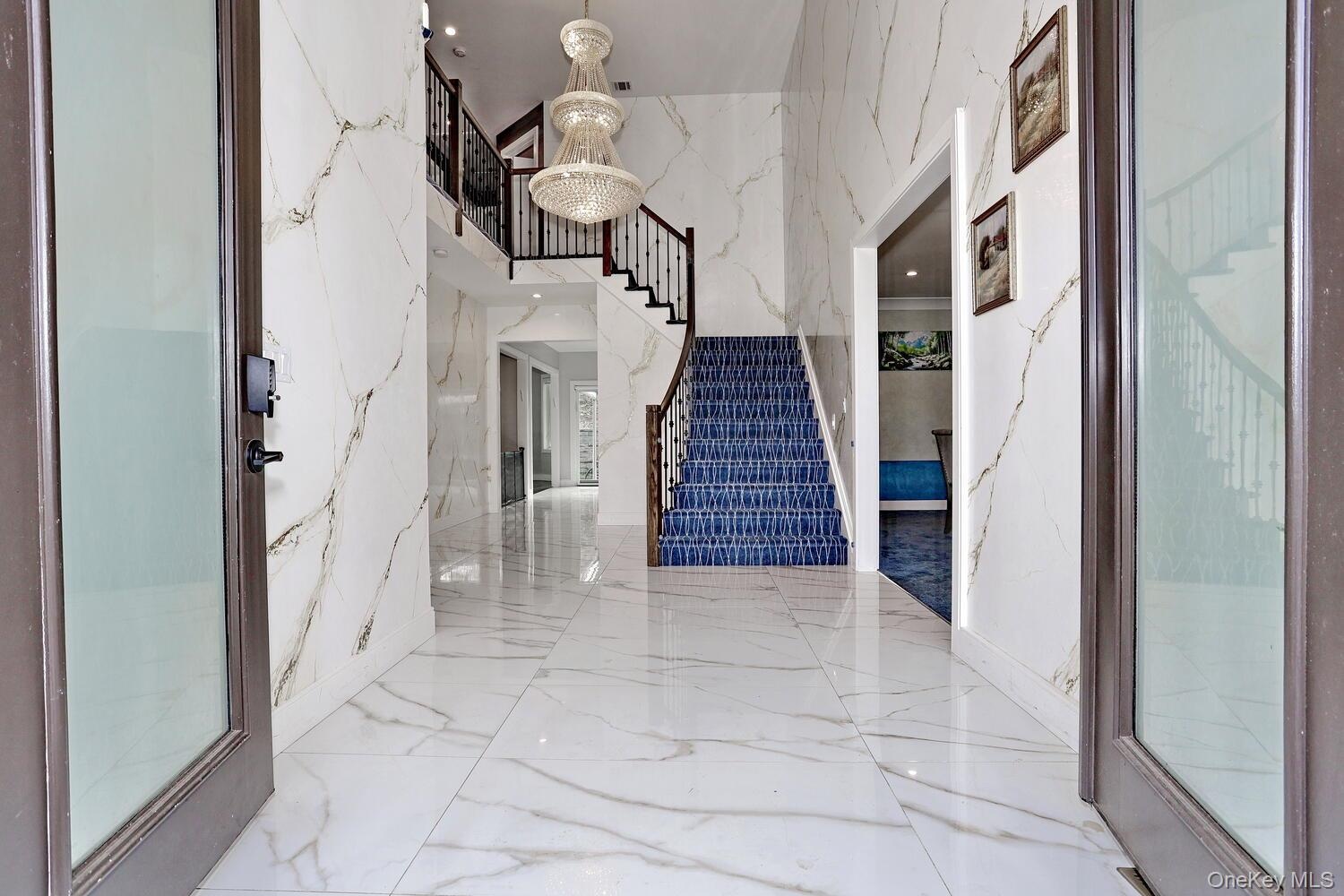 Foyer entrance with stairway, a chandelier, marble tiled flooring, a high ceiling, and stone wall