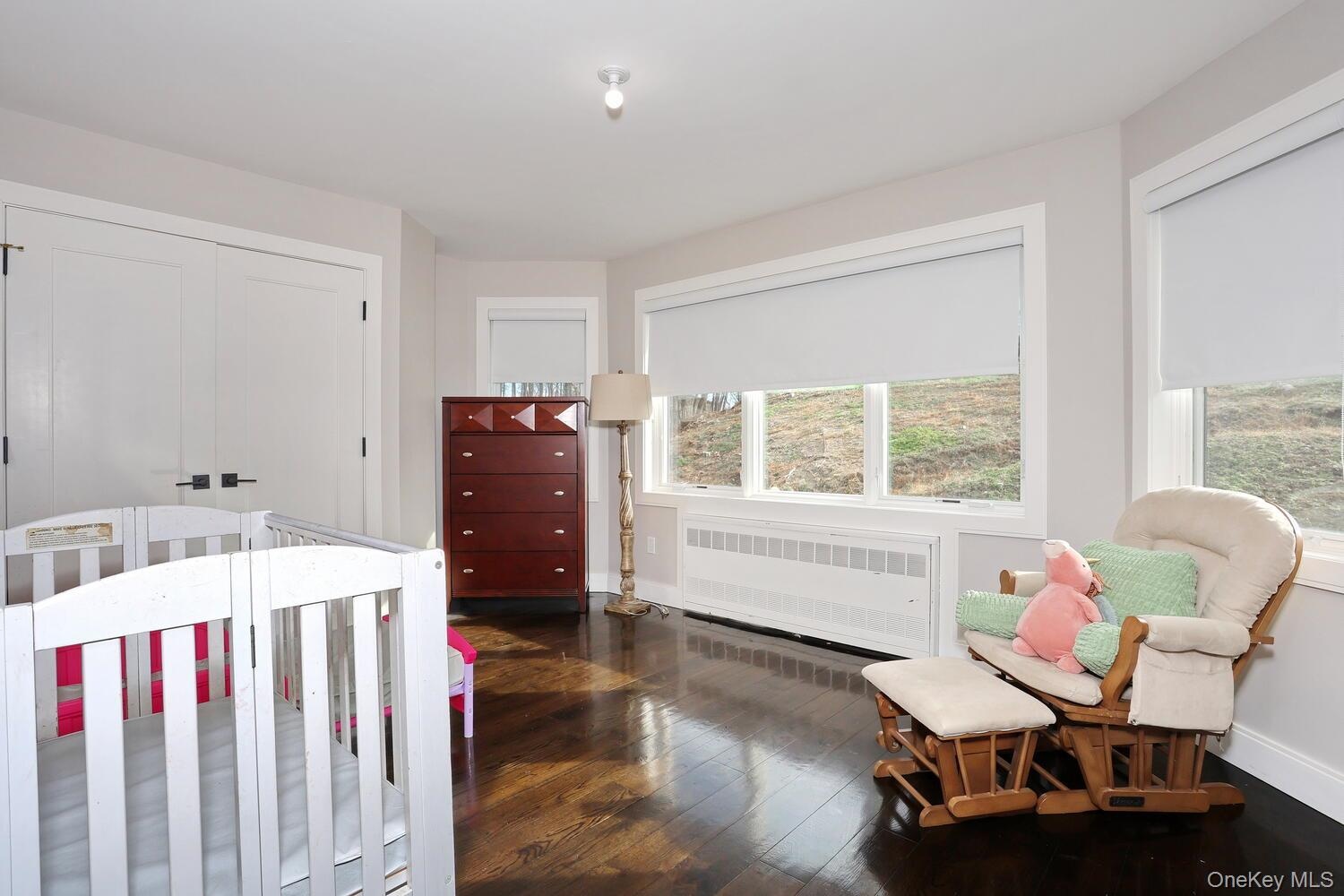 Bedroom featuring a nursery area, radiator, a closet, and dark wood-style floors