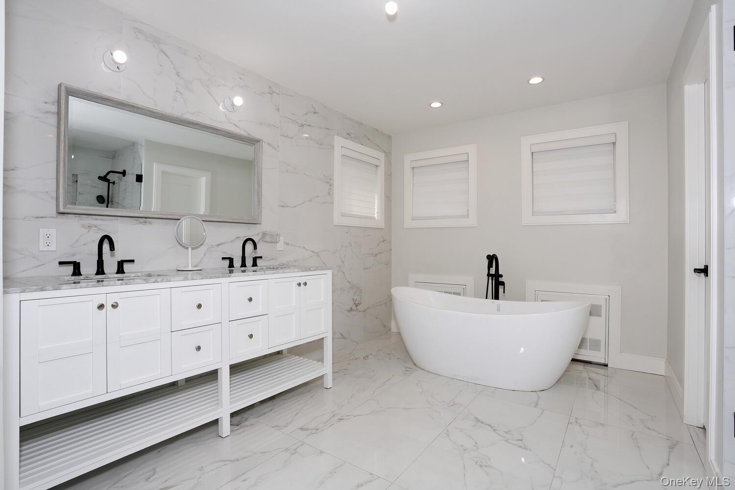 Bathroom featuring stone wall, a soaking tub, recessed lighting, double vanity, and light marble finish floors