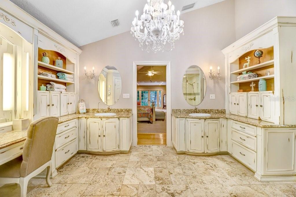 Vaulted ceilings in master bathroom with chandelier and his and her sink areas ample cabinetry for storage.