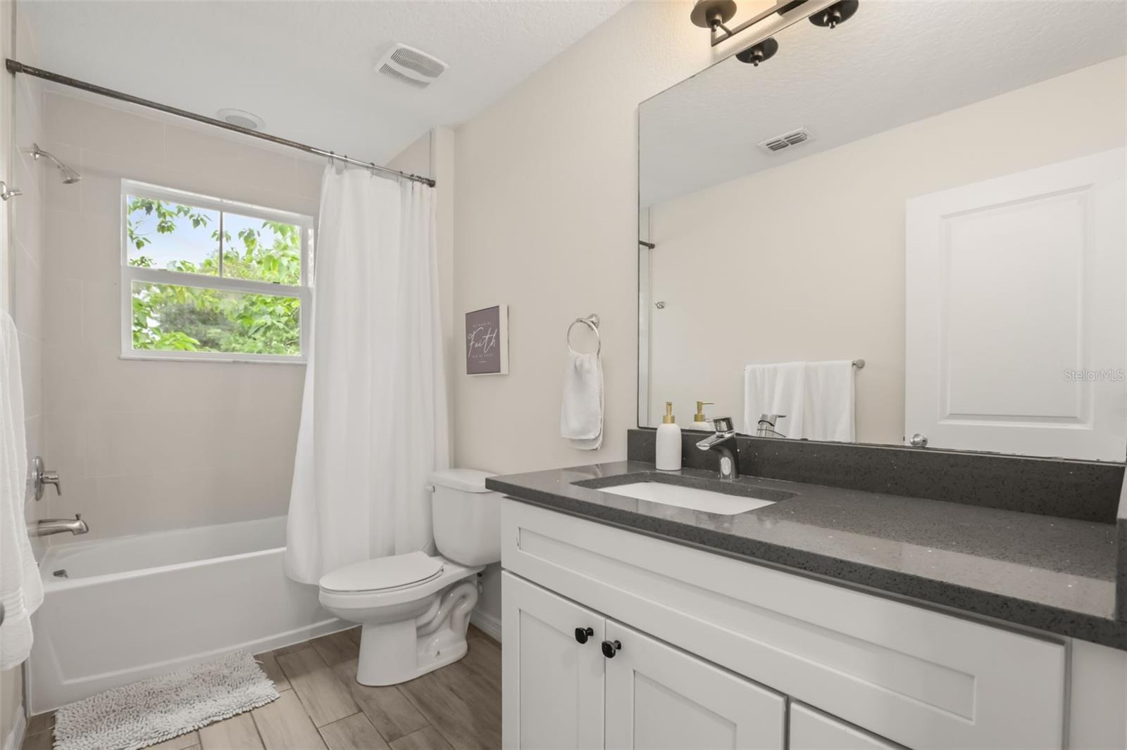 Bright guest bathroom featuring a single vanity, tub/shower combination, and a functional layout.