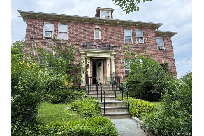Brick facade residence featuring a central dormer, multiple window units, and a stone pathway leading to the main entrance