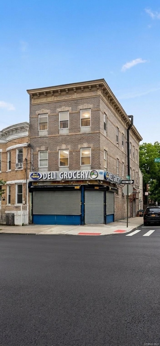 Three-story brick building featuring ground-floor commercial space with roll-down security gates and upper-level windows