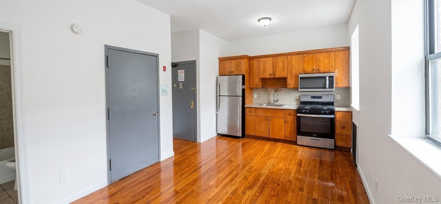Kitchen area featuring wood-finish flooring, light wood cabinetry, and stainless steel appliances including a refrigerator, range, and microwave