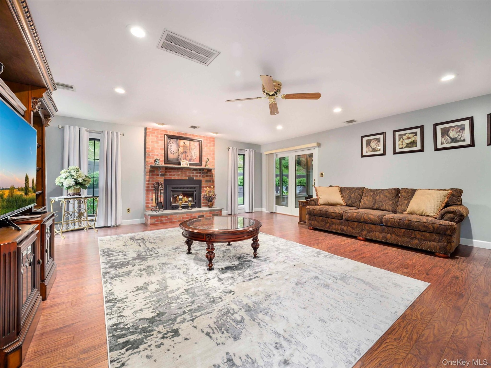 Spacious living area featuring a brick-surround fireplace with a stone hearth, wood-finish flooring, recessed lighting, and a ceiling fan