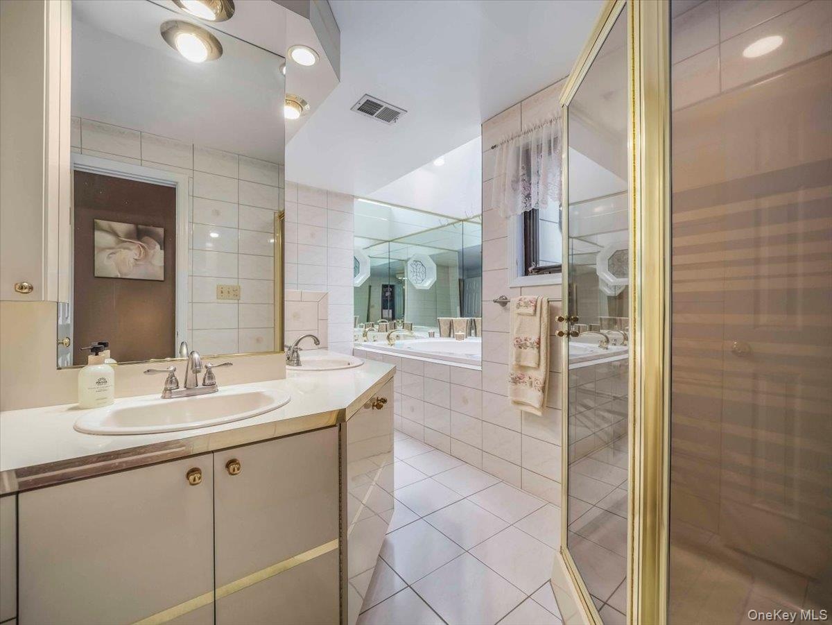 Bathroom featuring dual vanity with built-in storage, a tiled soaking tub, and a glass-enclosed shower