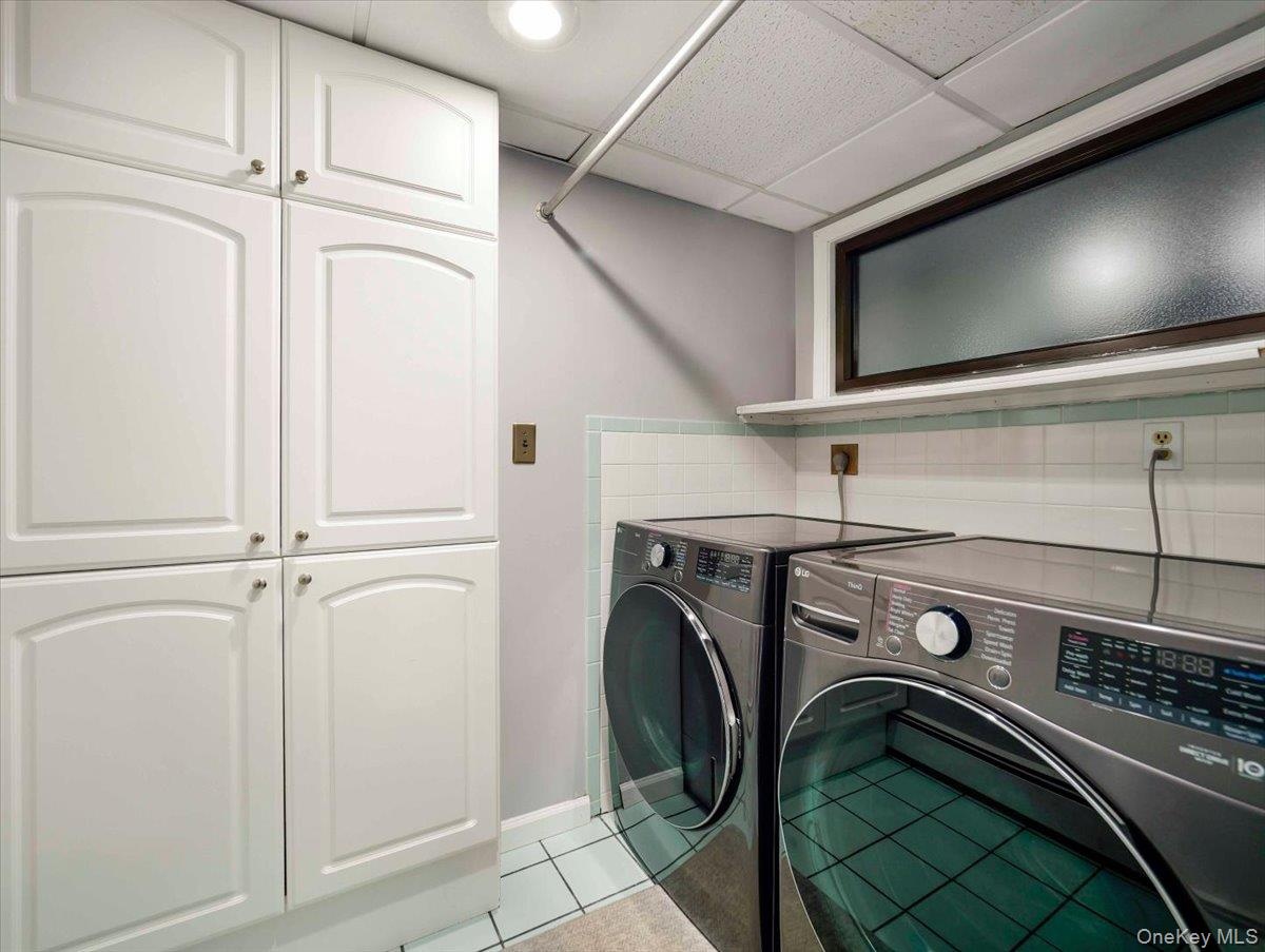 Laundry area with white paneled cabinetry, light blue wall tile, and frosted glass window