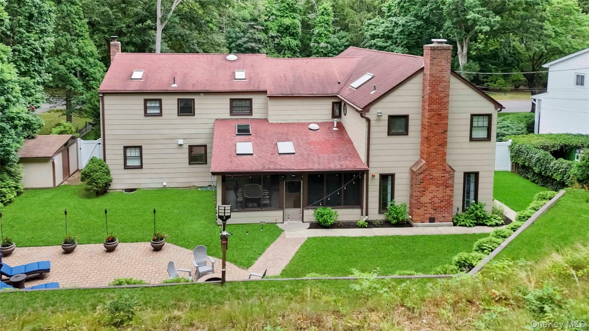 Expansive rear exterior featuring a red shingle roof with skylights, a screened porch, and a large paver patio