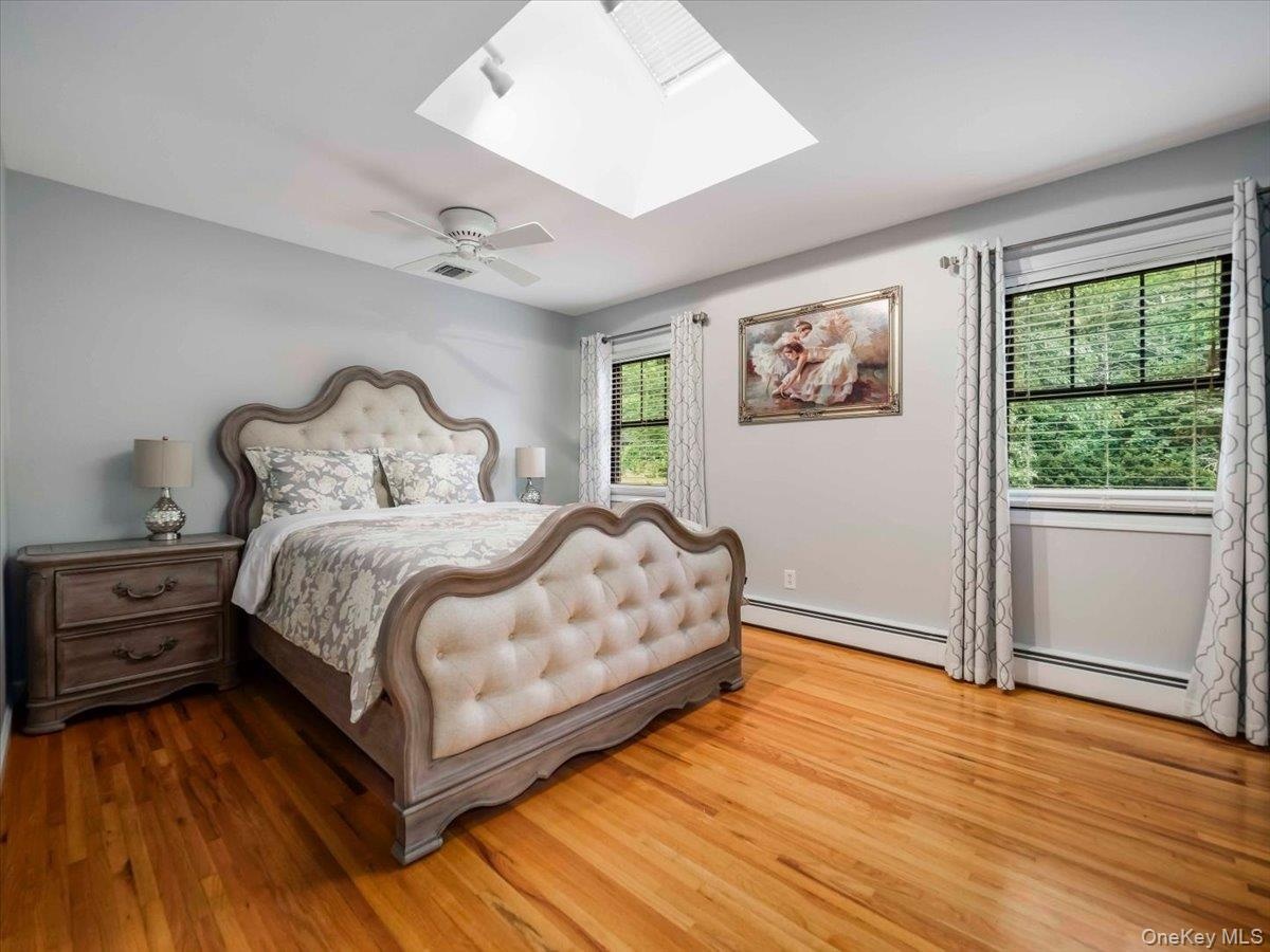 Room featuring hardwood flooring, a ceiling fan, and a skylight with integrated track lighting