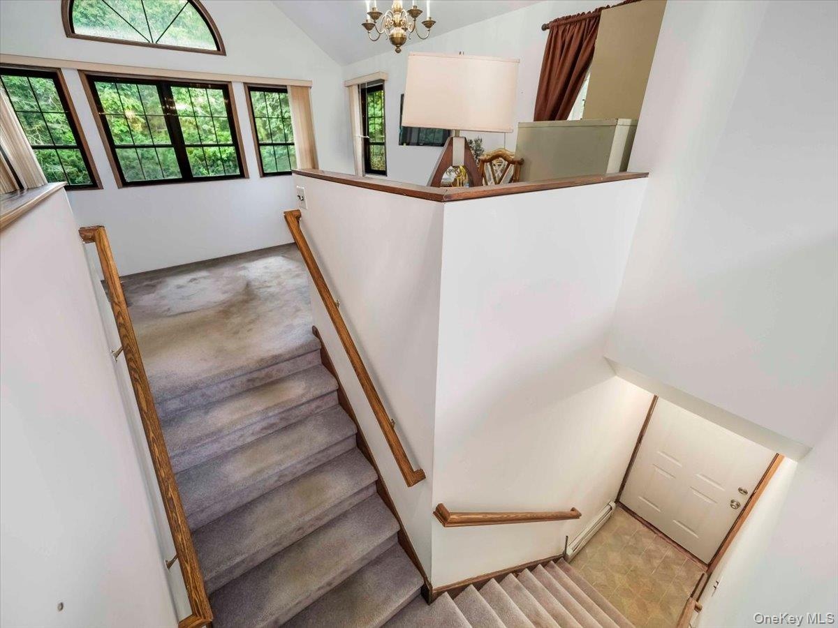 Multi-level interior featuring a carpeted staircase with wood railings, a vaulted ceiling, and multiple windows with dark frames