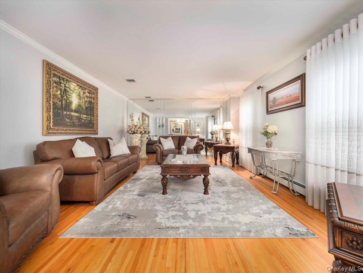 Spacious living area featuring polished wood-finish flooring, a decorative area rug, mirrored wall paneling, and crown molding