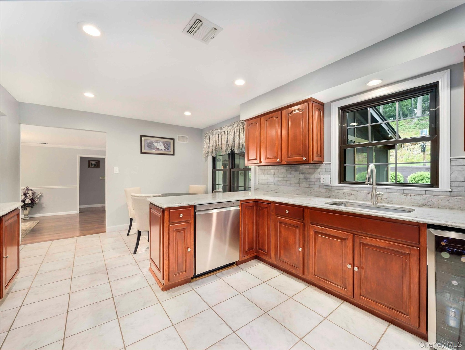 Kitchen featuring tiled flooring, wood cabinetry, stone countertops, a stainless steel dishwasher, and recessed lighting