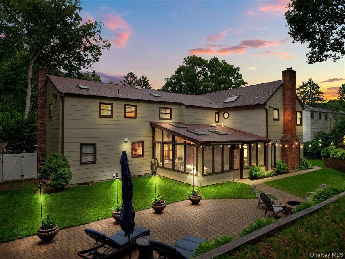 Expansive rear exterior featuring a paved patio and a glass-enclosed sunroom with skylights