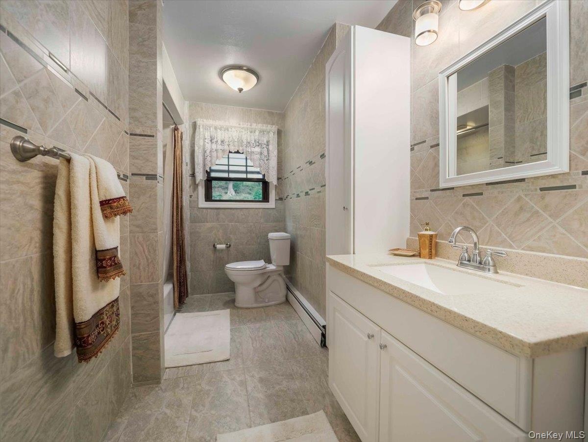 Full bathroom with a white vanity featuring a light-toned countertop, a framed mirror, and a white storage cabinet