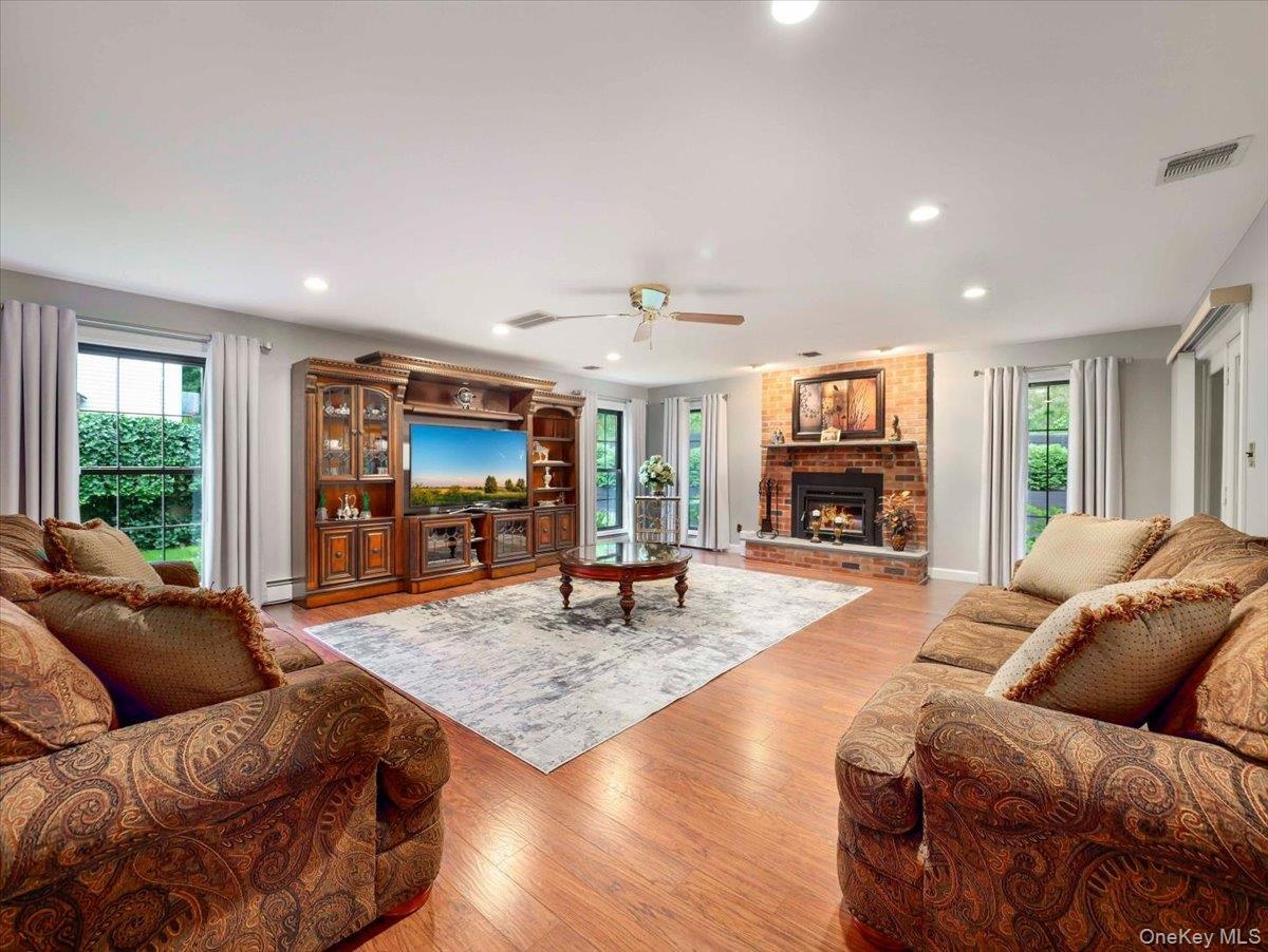 Spacious living area featuring wood-finish flooring, a prominent brick fireplace, and recessed lighting