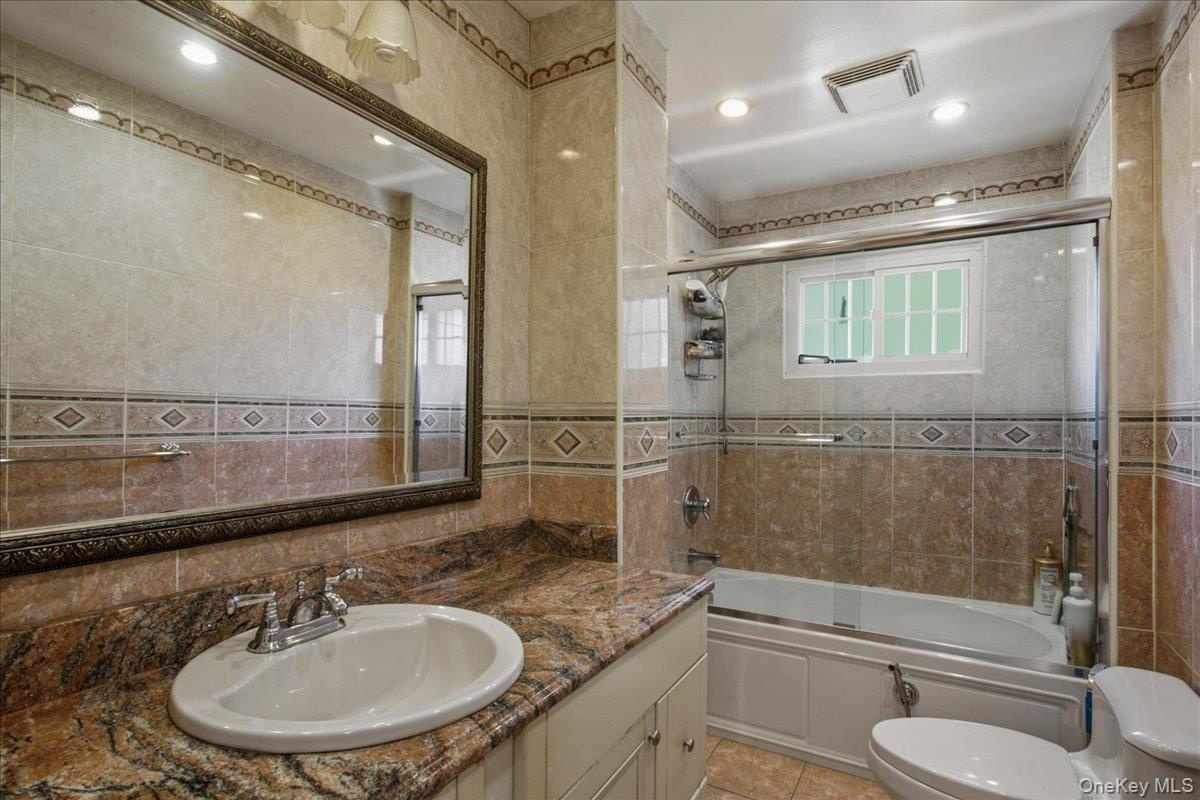 Hall bathroom featuring a built-in tub with glass enclosure, white framed window, and recessed lighting